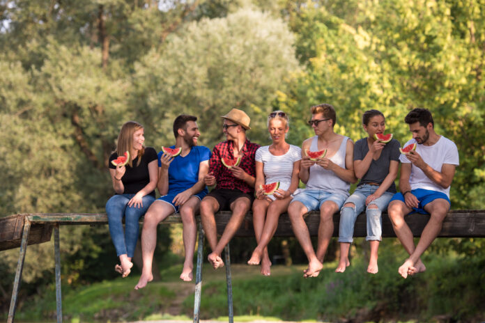 friends enjoying watermelon while sitting on the wooden bridge